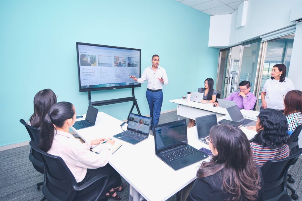 Team meeting at tables with a presenter at a large TV screen